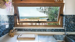 A kitchen with a large window overlooking a coastal view, a wooden cutting board, and a metal sink. - Casa Azul, Seaview terrace, private parking, pool (Golfo Aranci)