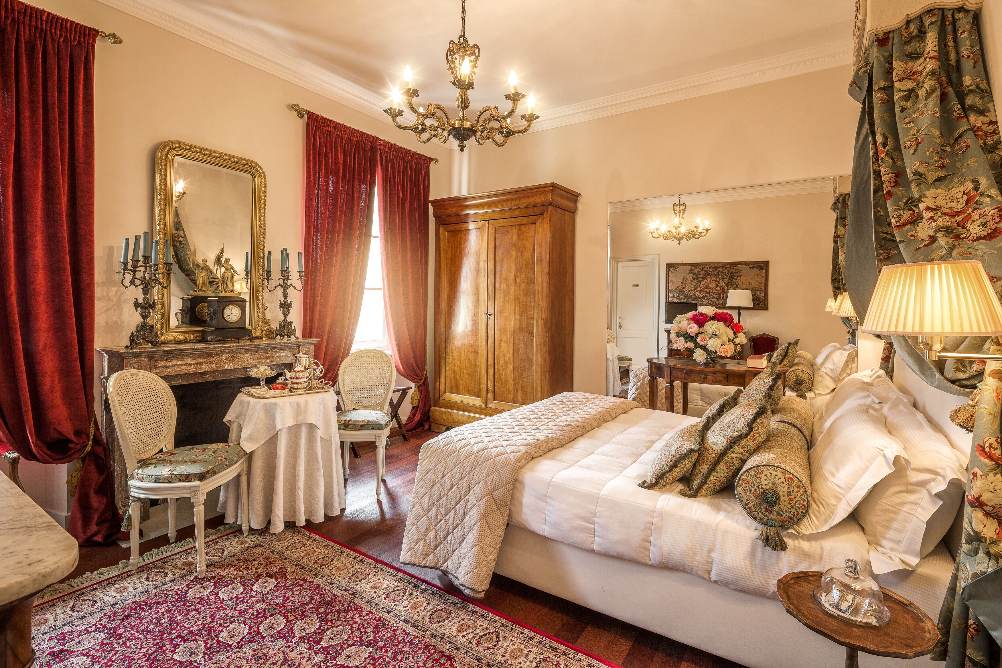 A bedroom with a large bed, a wooden wardrobe, a mirror, and a chandelier.