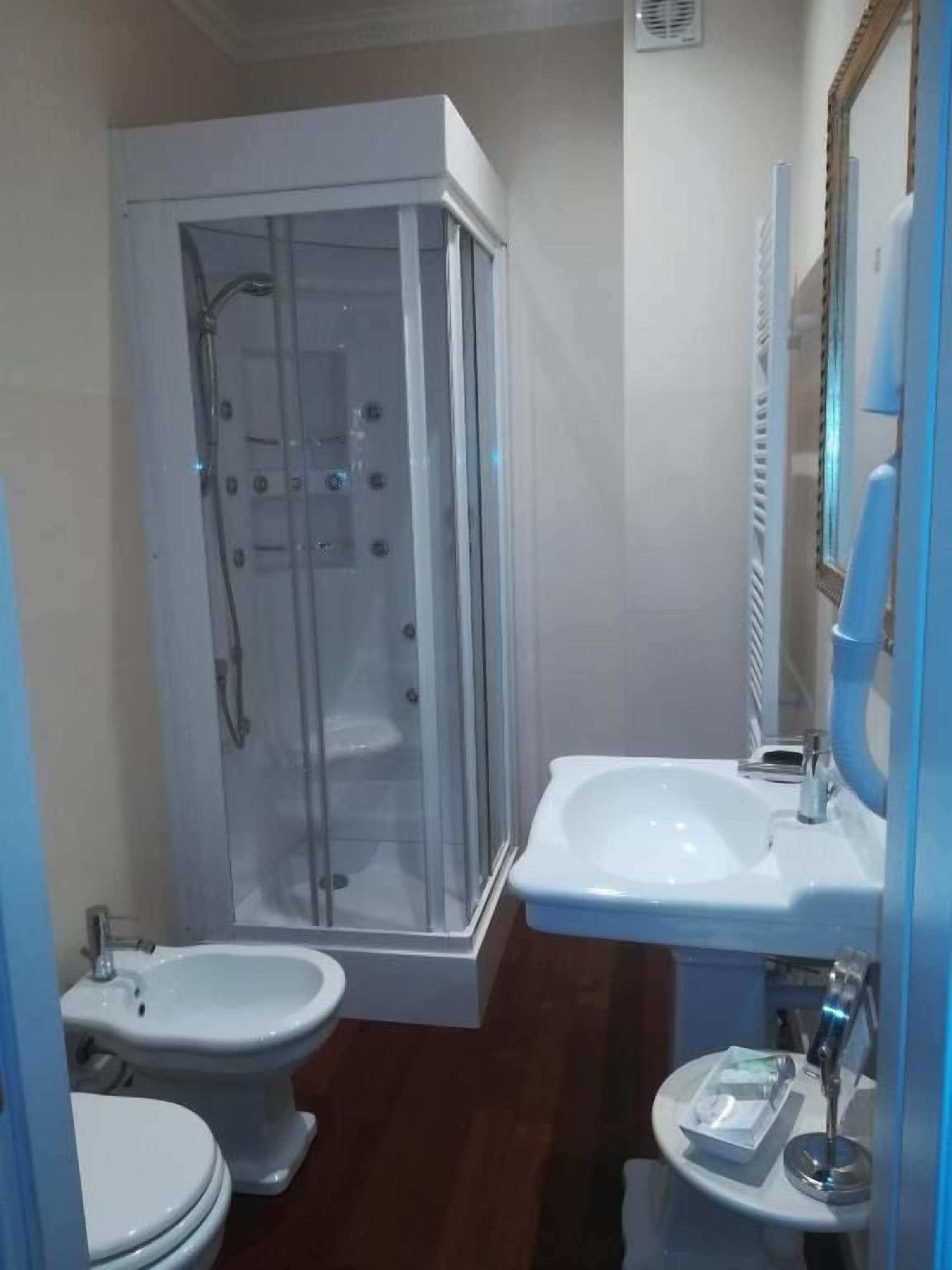 Une salle de bain avec une douche à parois de verre, un lavabo blanc et deux toilettes.