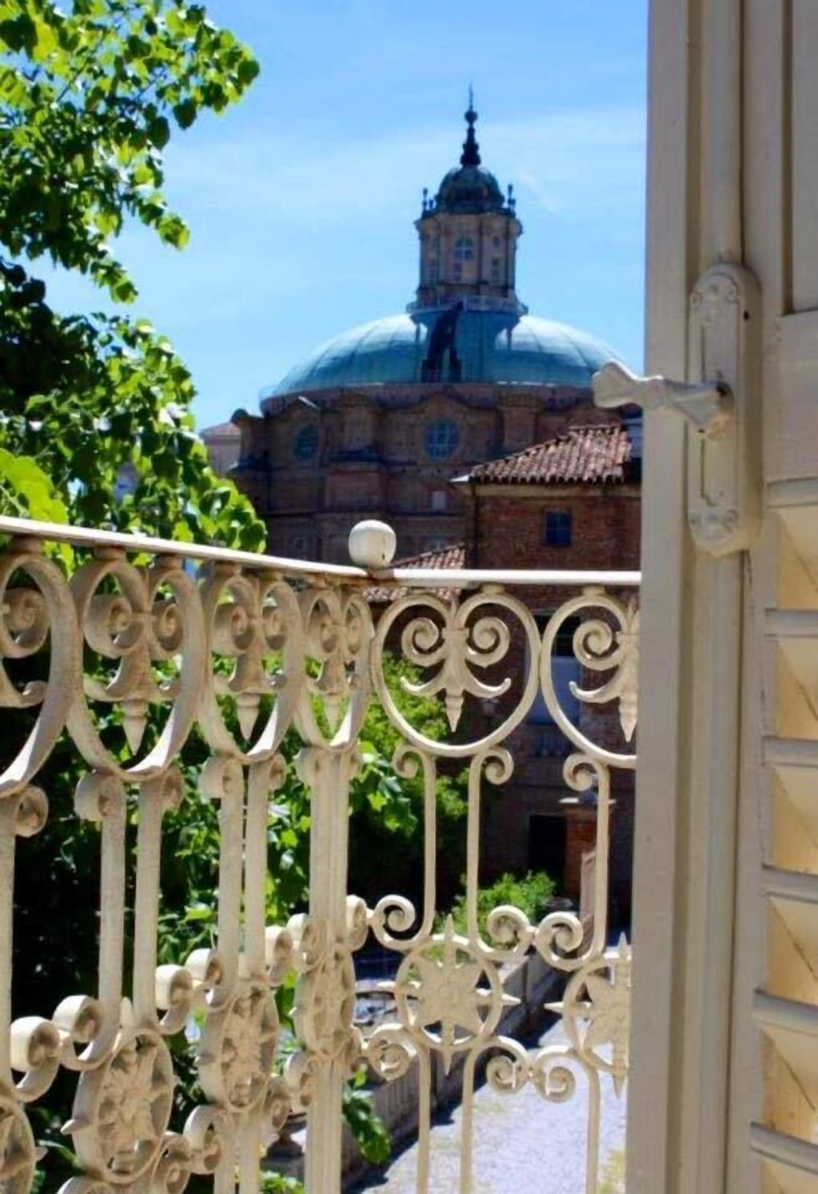 A balcony with ornate metal railings overlooking a building with a dome and a tower.