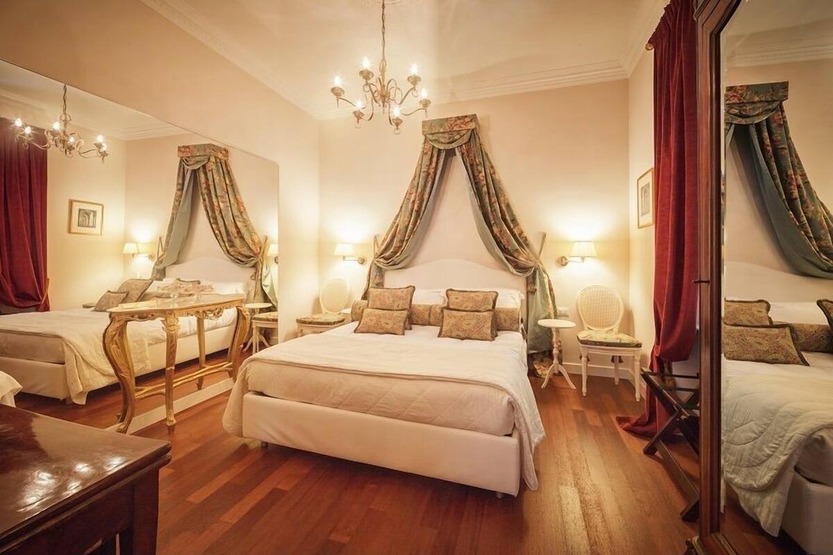 A luxurious bedroom with a large bed, two bedside tables, a chandelier, and draped curtains.