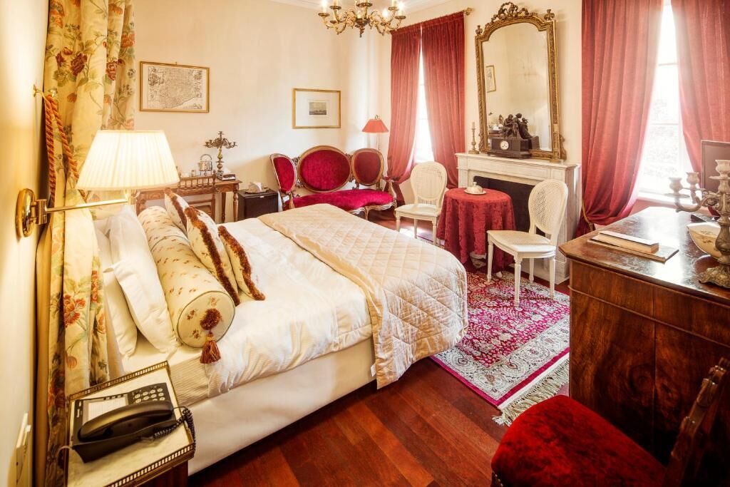 A hotel room with a bed, a desk, a chair, a fireplace, and a large mirror.