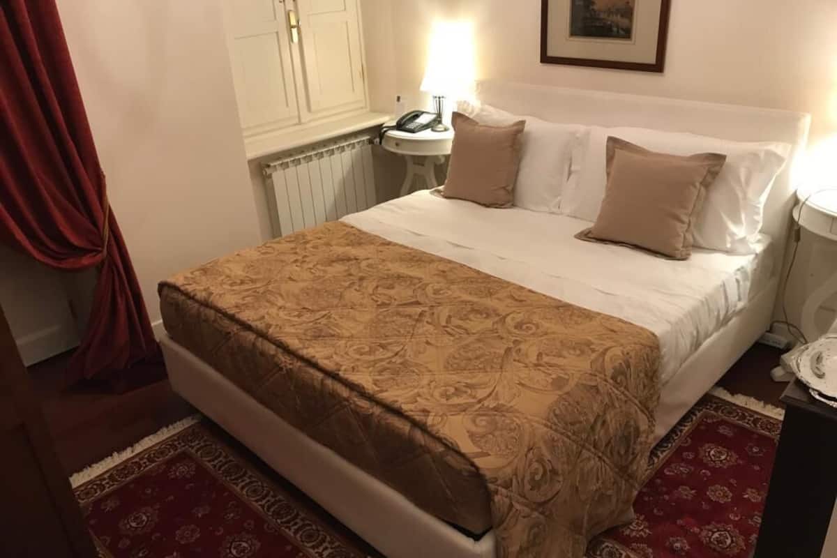 A neatly made bed with a patterned bedspread, a bedside table with a lamp, and a red patterned rug.