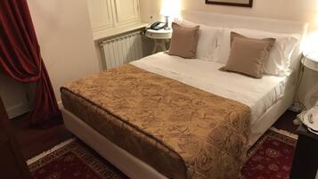 A neatly made bed with a patterned bedspread, a bedside table with a lamp, and a red patterned rug.
