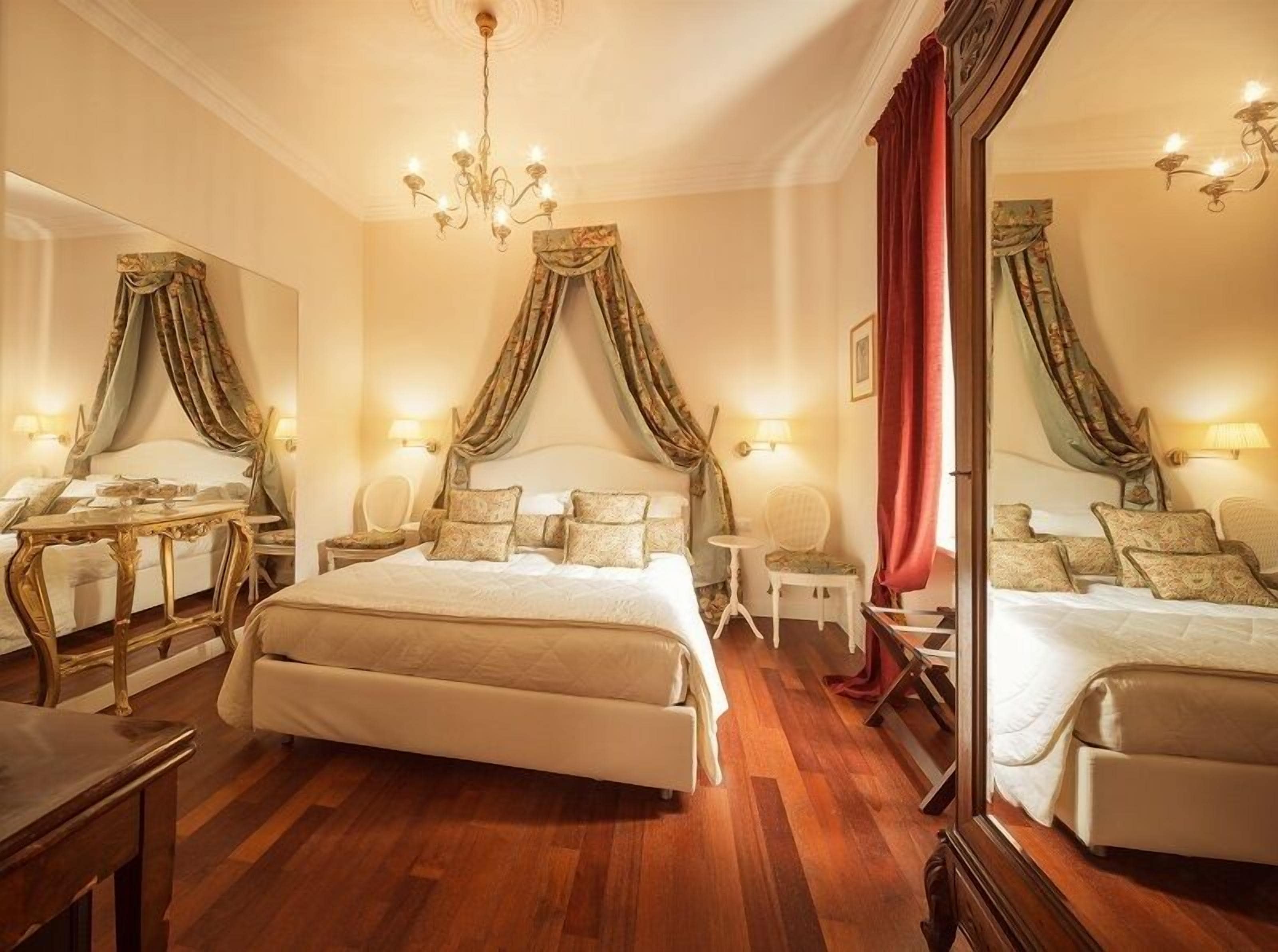 A luxurious bedroom with a large bed, a mirror, a chandelier, and a wooden floor.