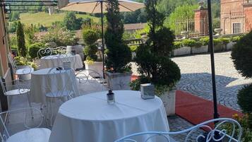 An outdoor patio with round tables and white metal chairs, surrounded by beige umbrellas.