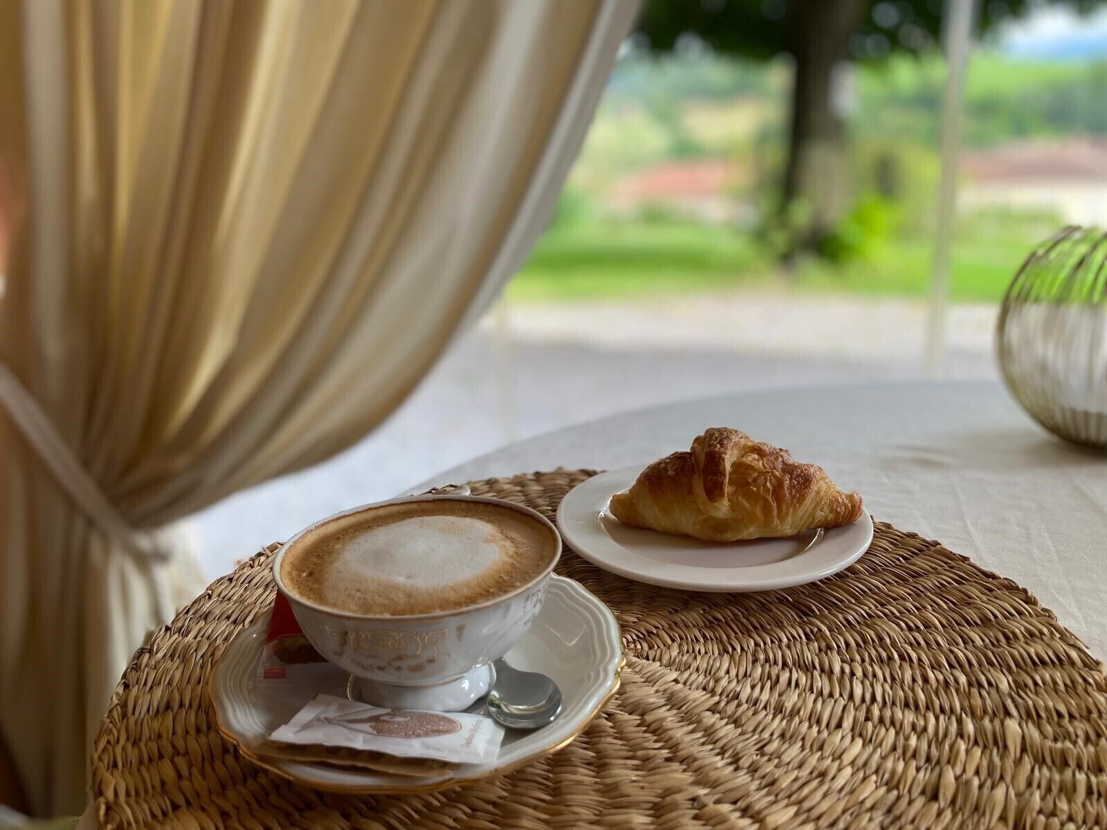 A wicker table with a cup of coffee and a croissant.