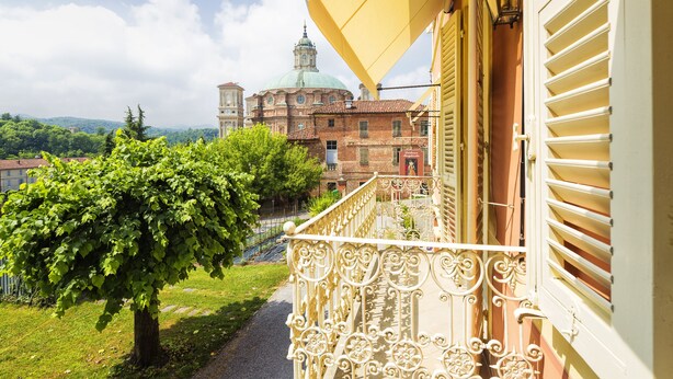 A balcony with ornate metal railings overlooking a tree-lined path and a historic building with a dome. - Duchessa Margherita (Vicoforte)