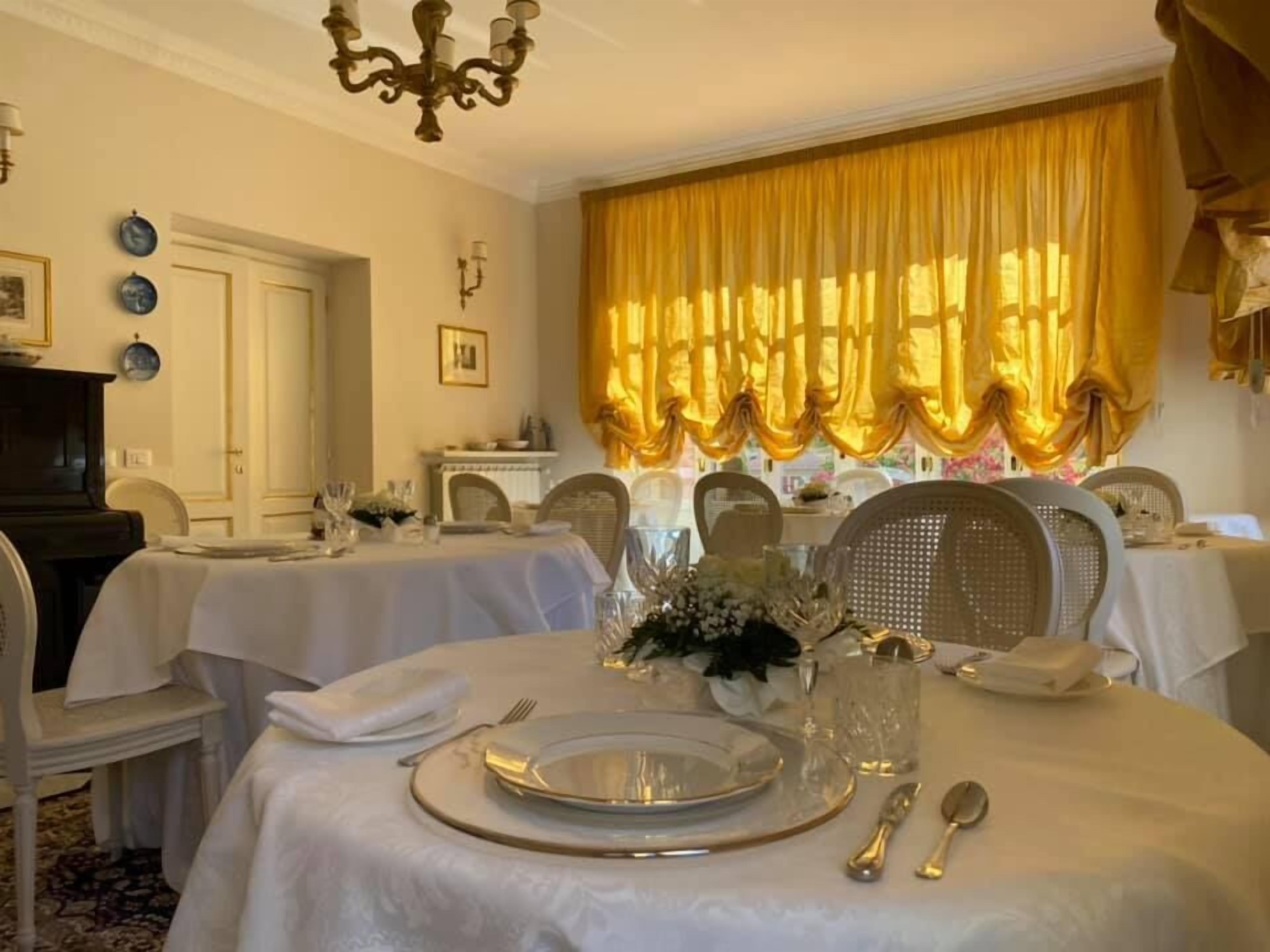 Una sala da pranzo con tavoli rotondi per quattro persone, ognuno con tovaglia bianca, posateria e bicchieri.