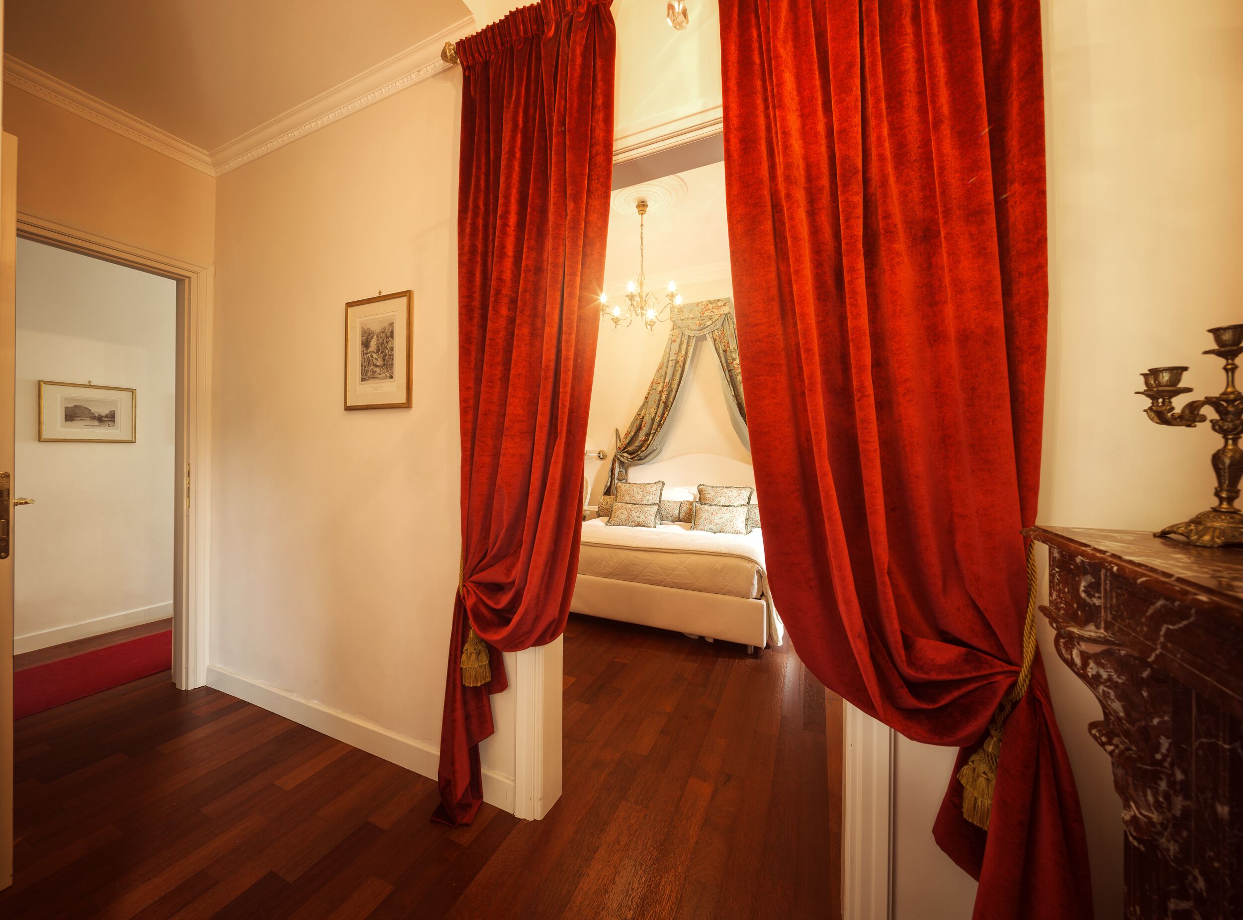 A room with a bed, a chandelier, and red curtains.