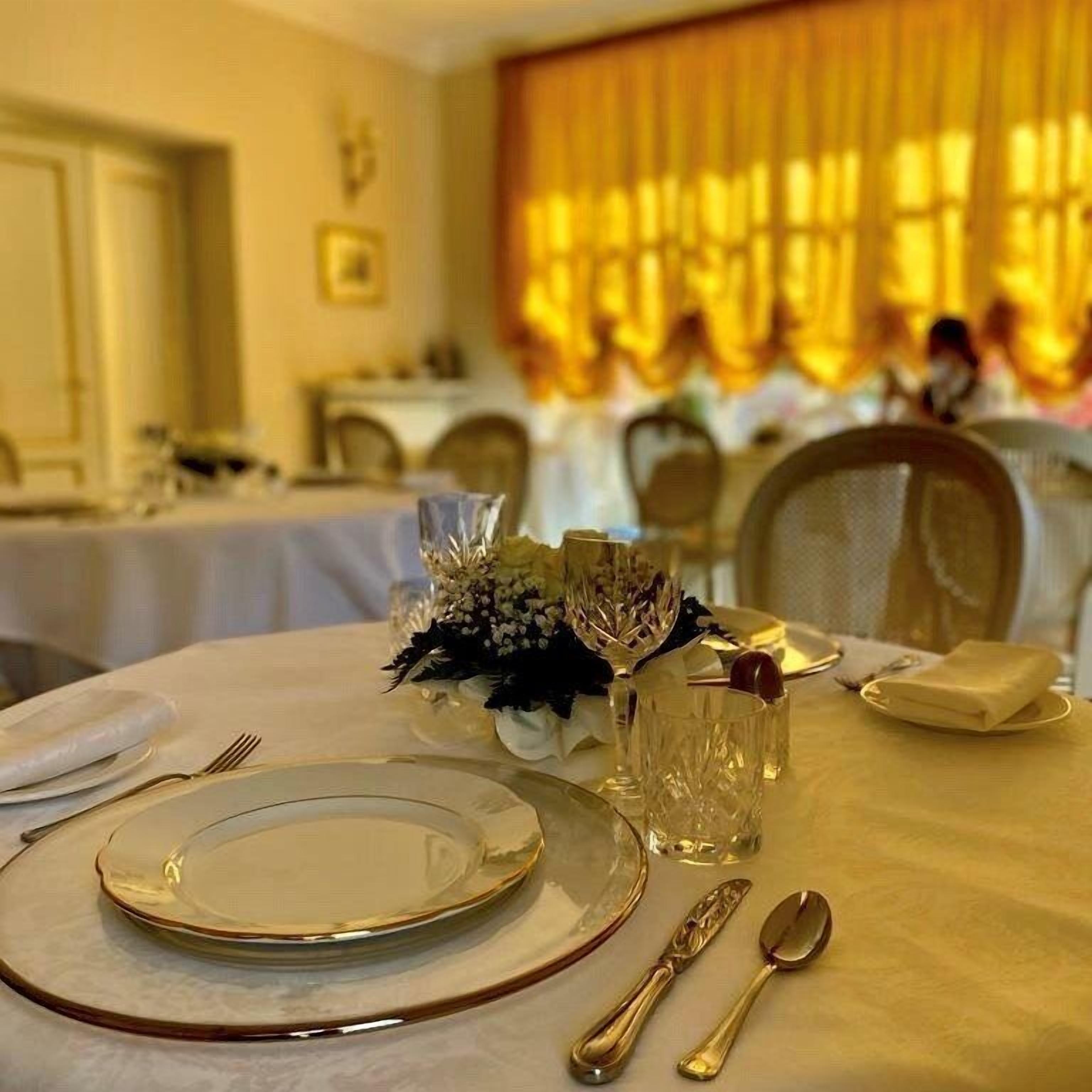 A dining table set with plates, cutlery, and a glass vase with flowers.