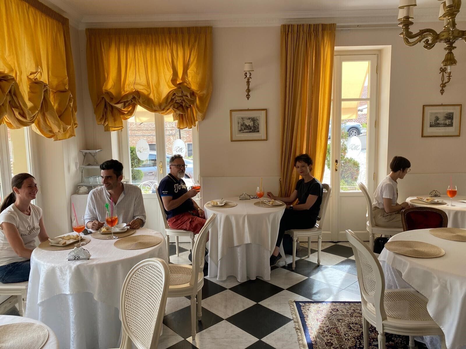 Comedor con mesas redondas, sillas blancas y cortinas amarillas.