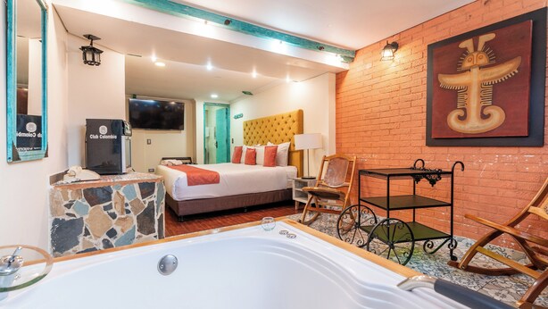 Hotelkamer met een groot bad, een bed met een gestuufd hoofdeinde, een houten stoel, een bijzettafeltje en een televisie aan de muur.