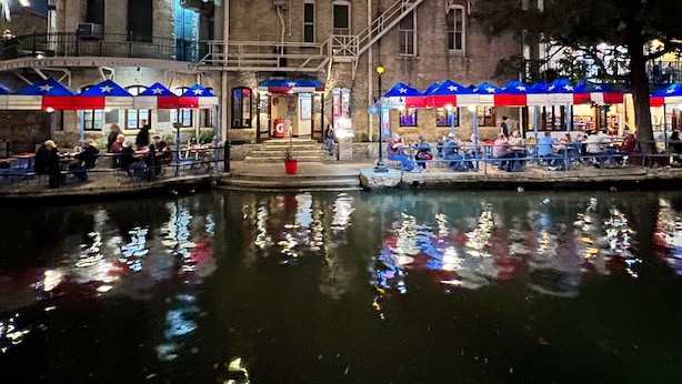 Un edificio frente al agua, con varios niveles y terrazas al aire libre, reflejado en el agua.