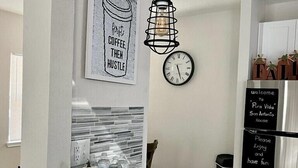 Una cocina con encimera de mármol, un cuadro con temática de café, una lámpara colgante y un letrero de bienvenida en el refrigerador.