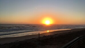 Ein Sonnenuntergang über einem Strand mit Wellen, einem Zaun und einem klaren Himmel.