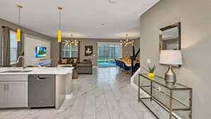 A modern kitchen with a built-in dishwasher, a dining area with a glass table, and a living room with a sofa and TV.
