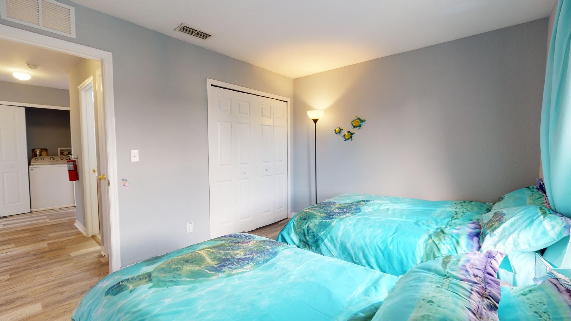 A bedroom with two beds, a closet, and a kitchenette in the background.