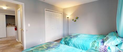 A bedroom with two beds, a closet, and a kitchenette in the background.