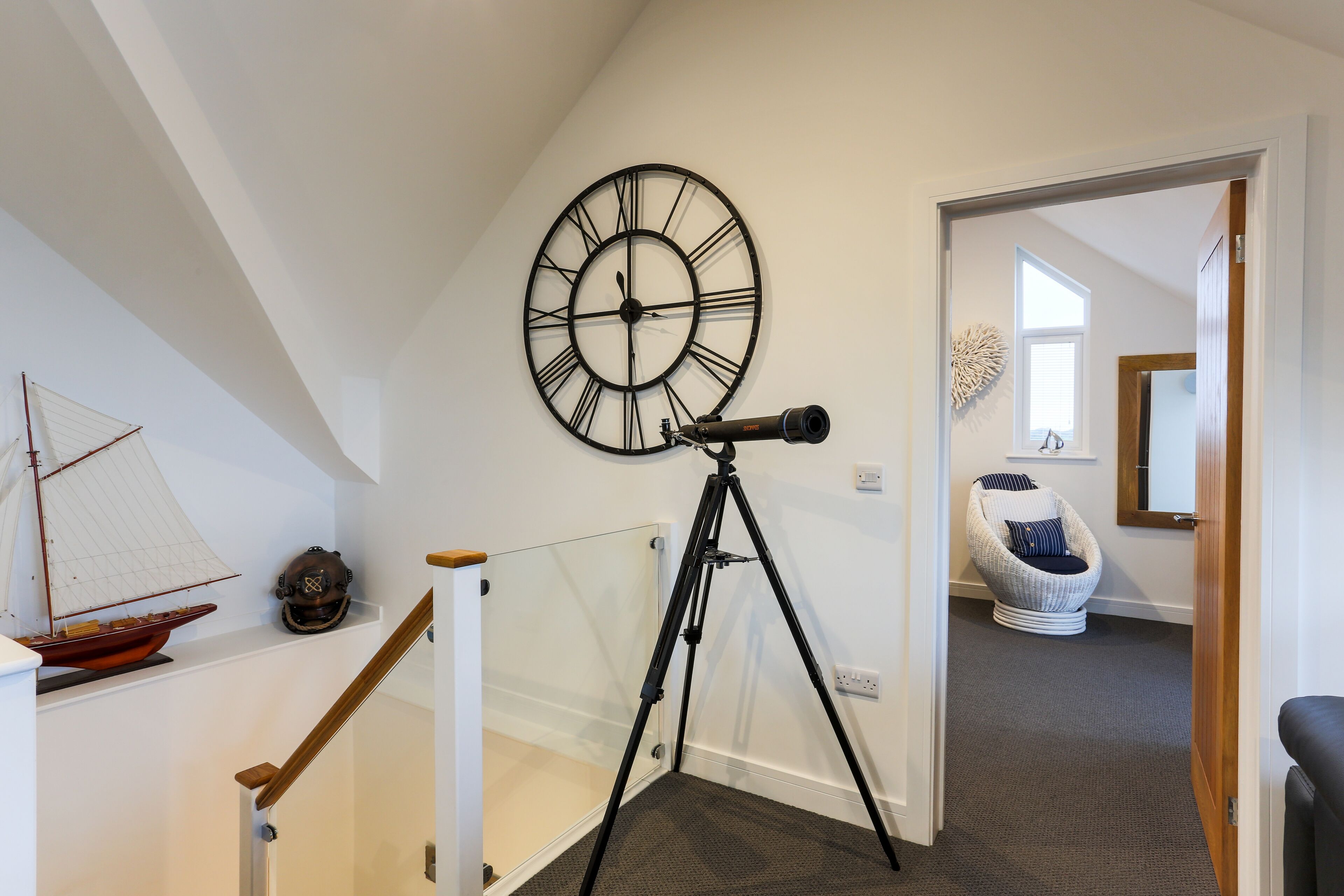 Un escalier avec une rampe en verre, un télescope fixé au mur, un modèle de bateau et un élément décoratif mural.
