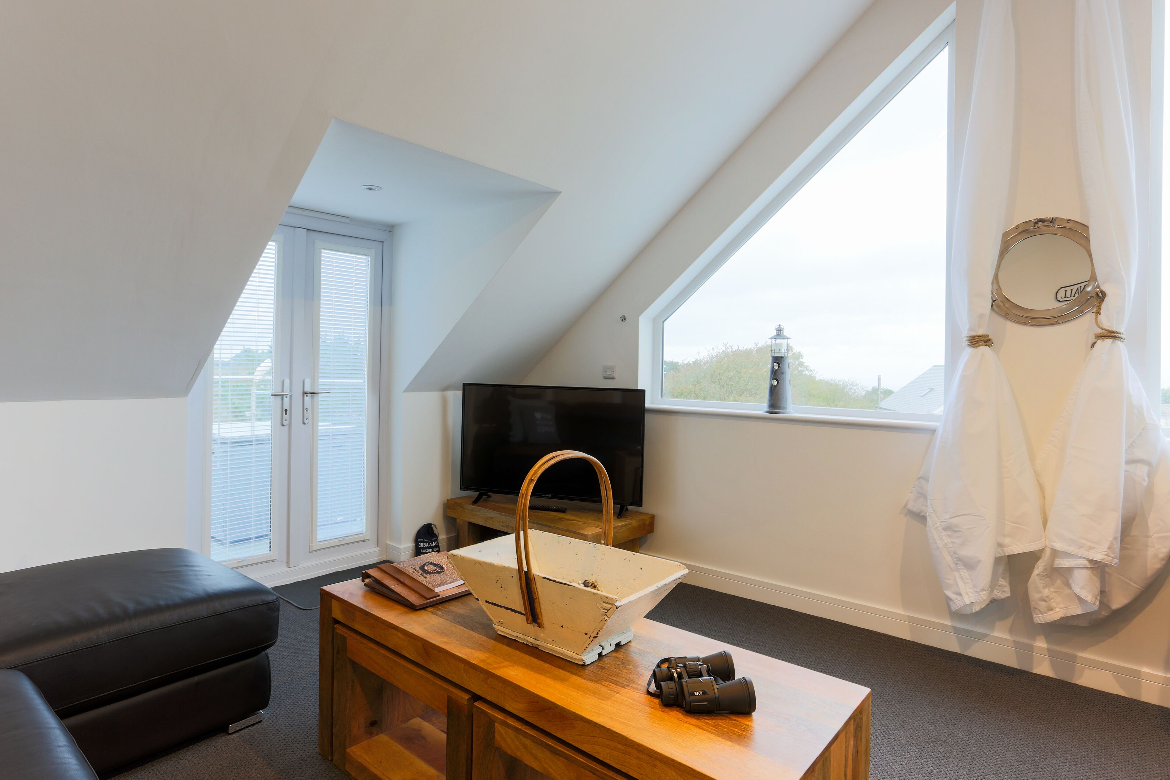 A modern room with a sloped ceiling, a television, a wooden side table, a camera, and a window with curtains.
