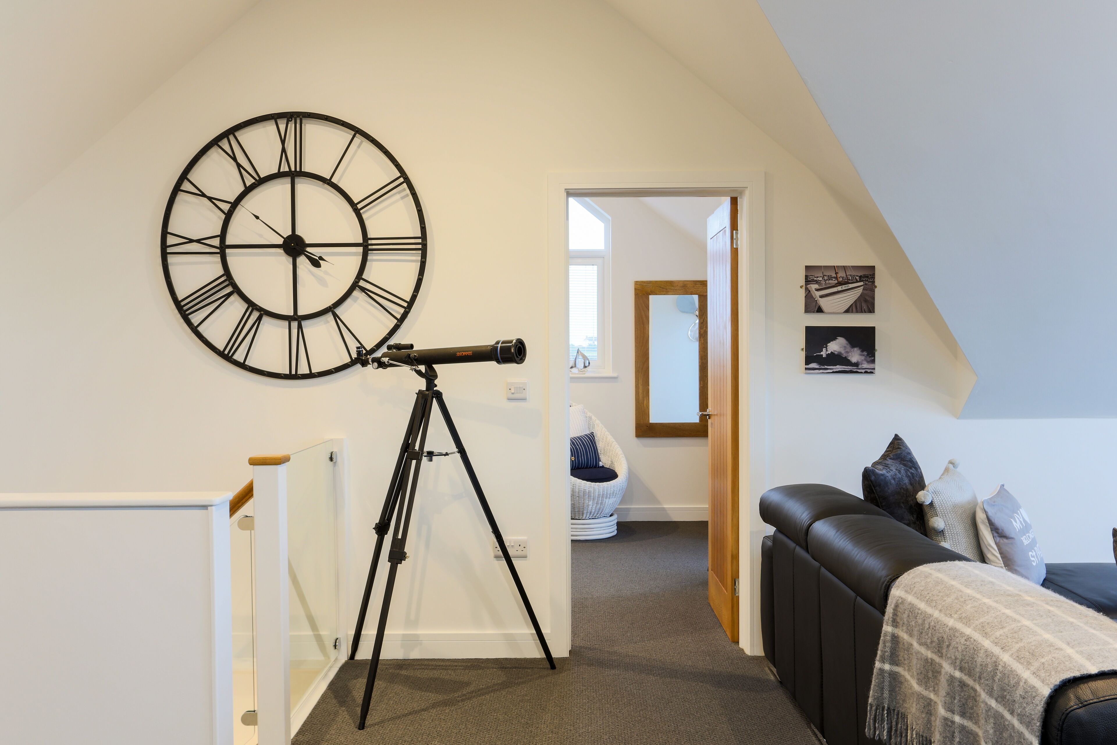 Une pièce avec une grande horloge murale, un télescope, un canapé en cuir noir et une vue sur l’extérieur par une porte.