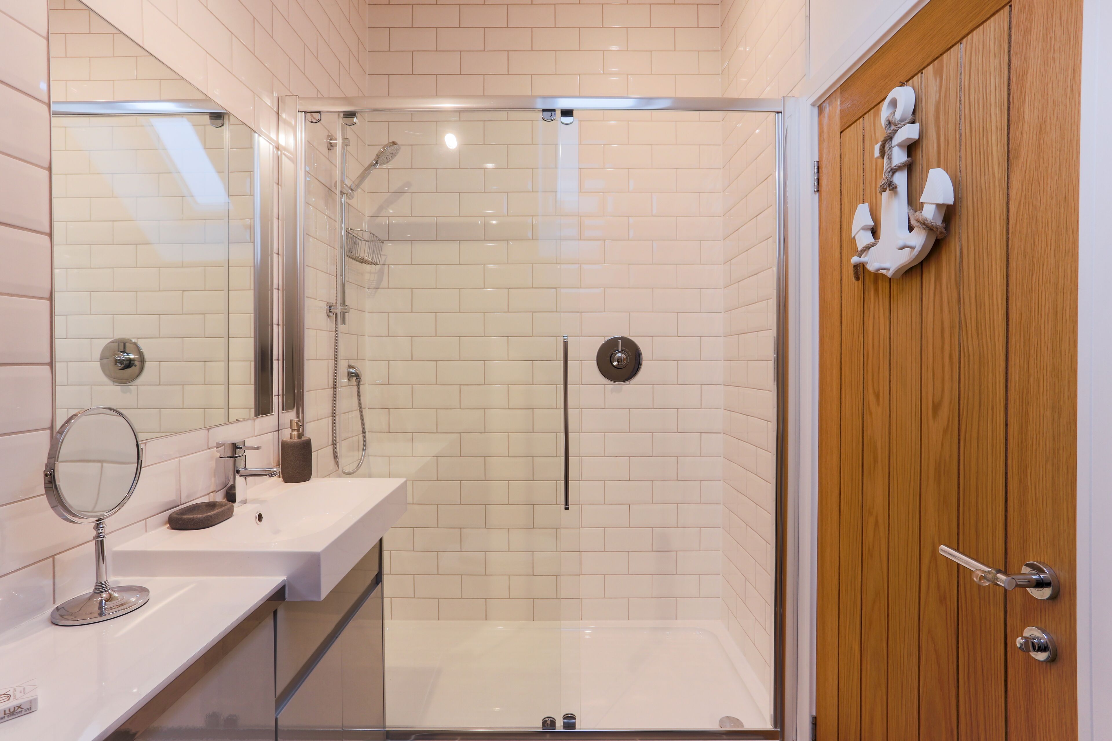 Un baño moderno con ducha envuelta en vidrio, puerta de madera y pared de azulejos blancos.