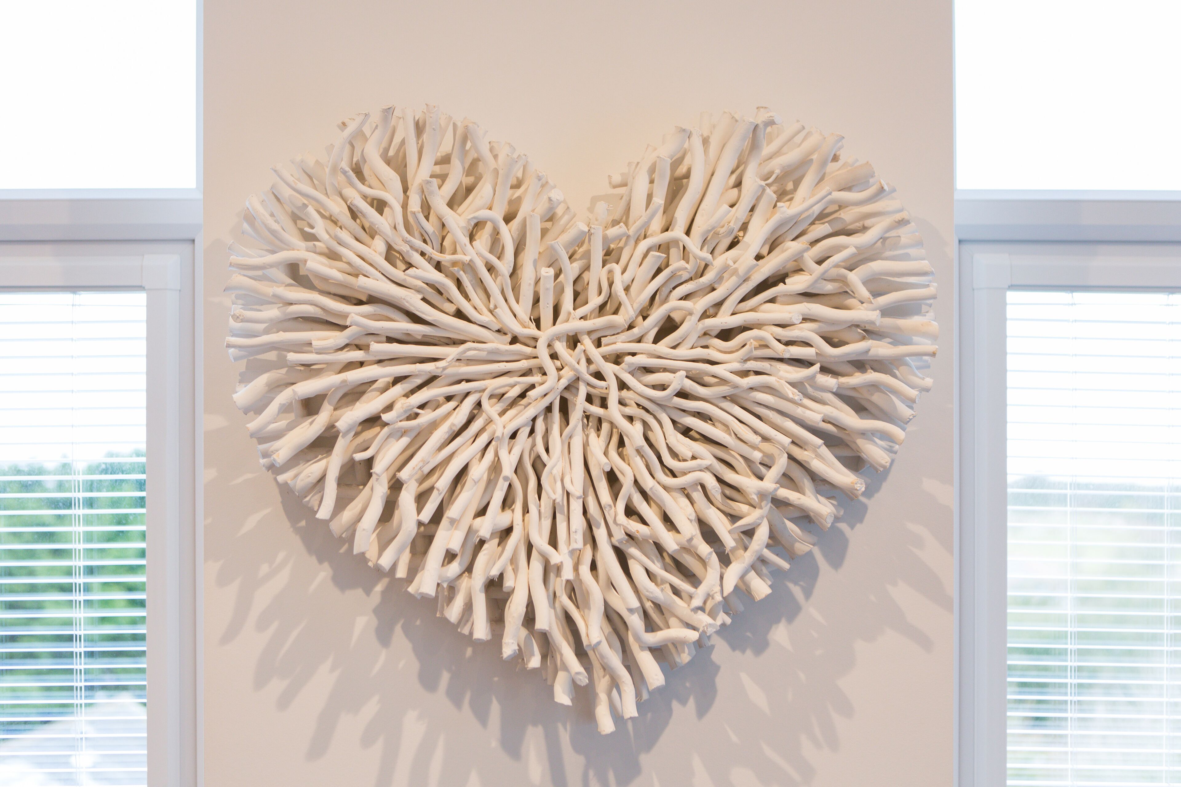 A heart-shaped wall art installation in a room with large windows and blinds.