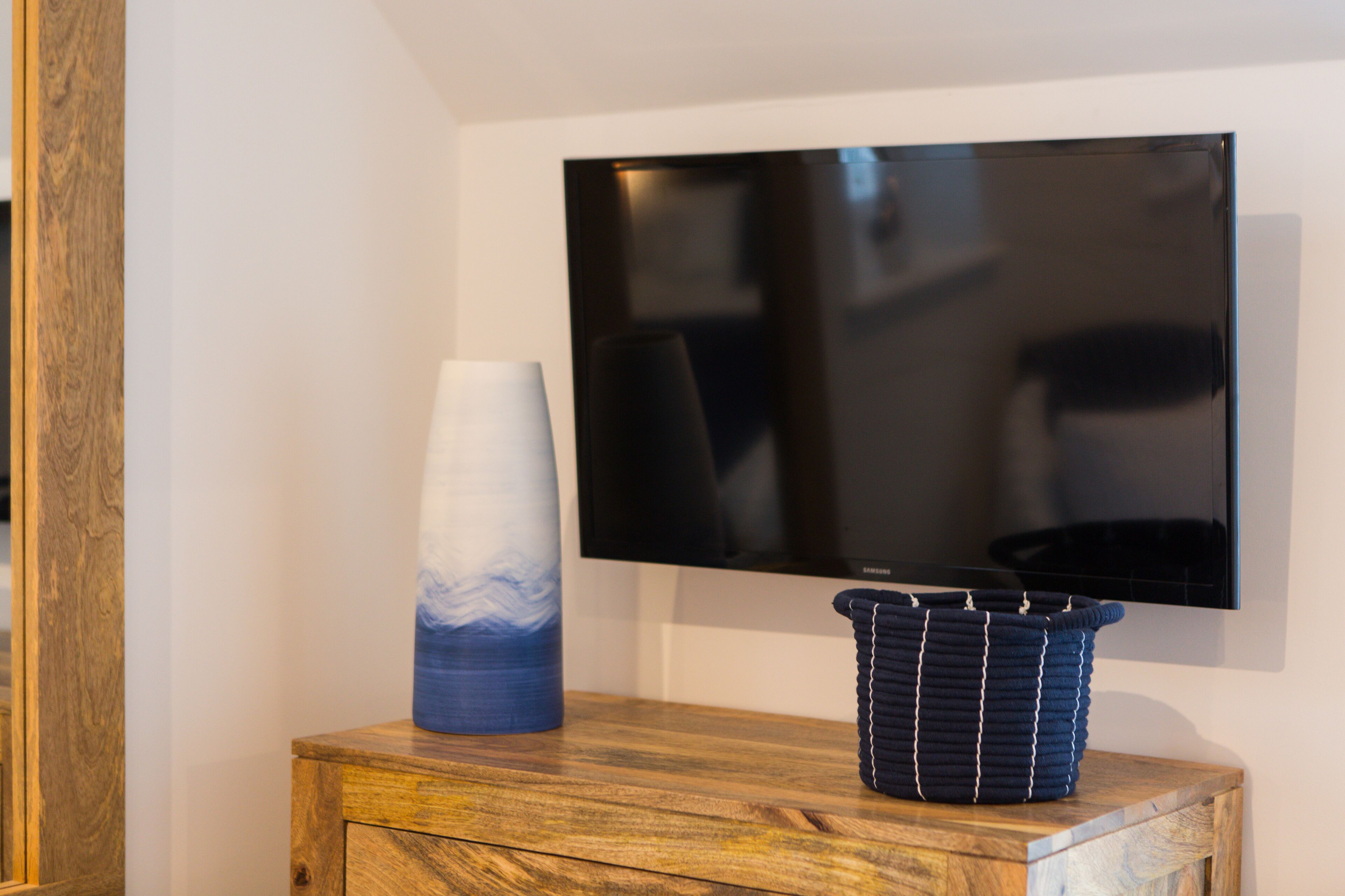 Un mobiletto in legno con un vaso e un cesto di vimini sopra.