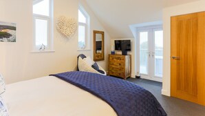 A bedroom with a large bed, a dresser, a television, and a door leading to a balcony. - The Lighthouse (St Ives)