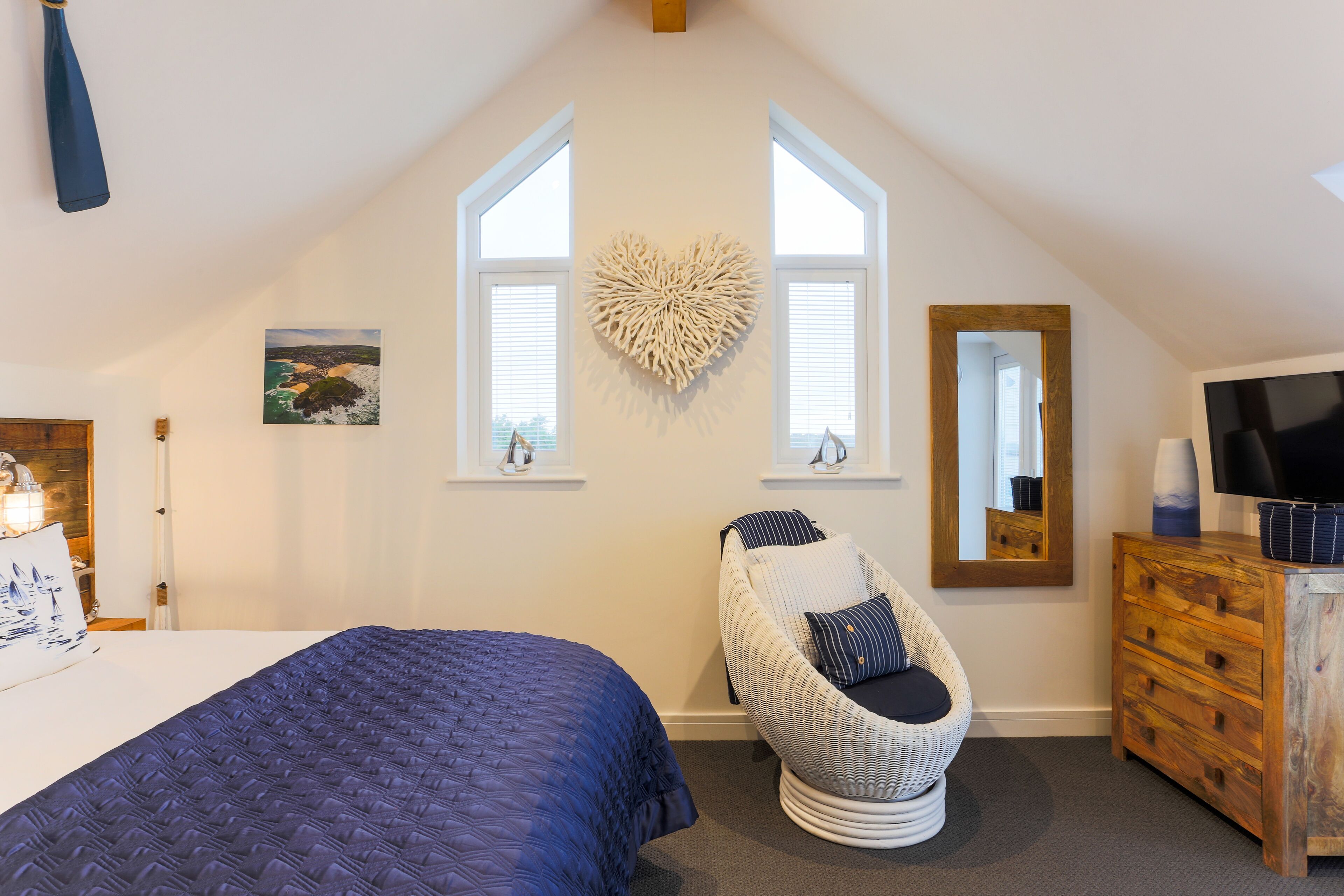 Une chambre avec un grand lit, une chaise, une commode et un élément décoratif en forme de cœur accroché au mur.
