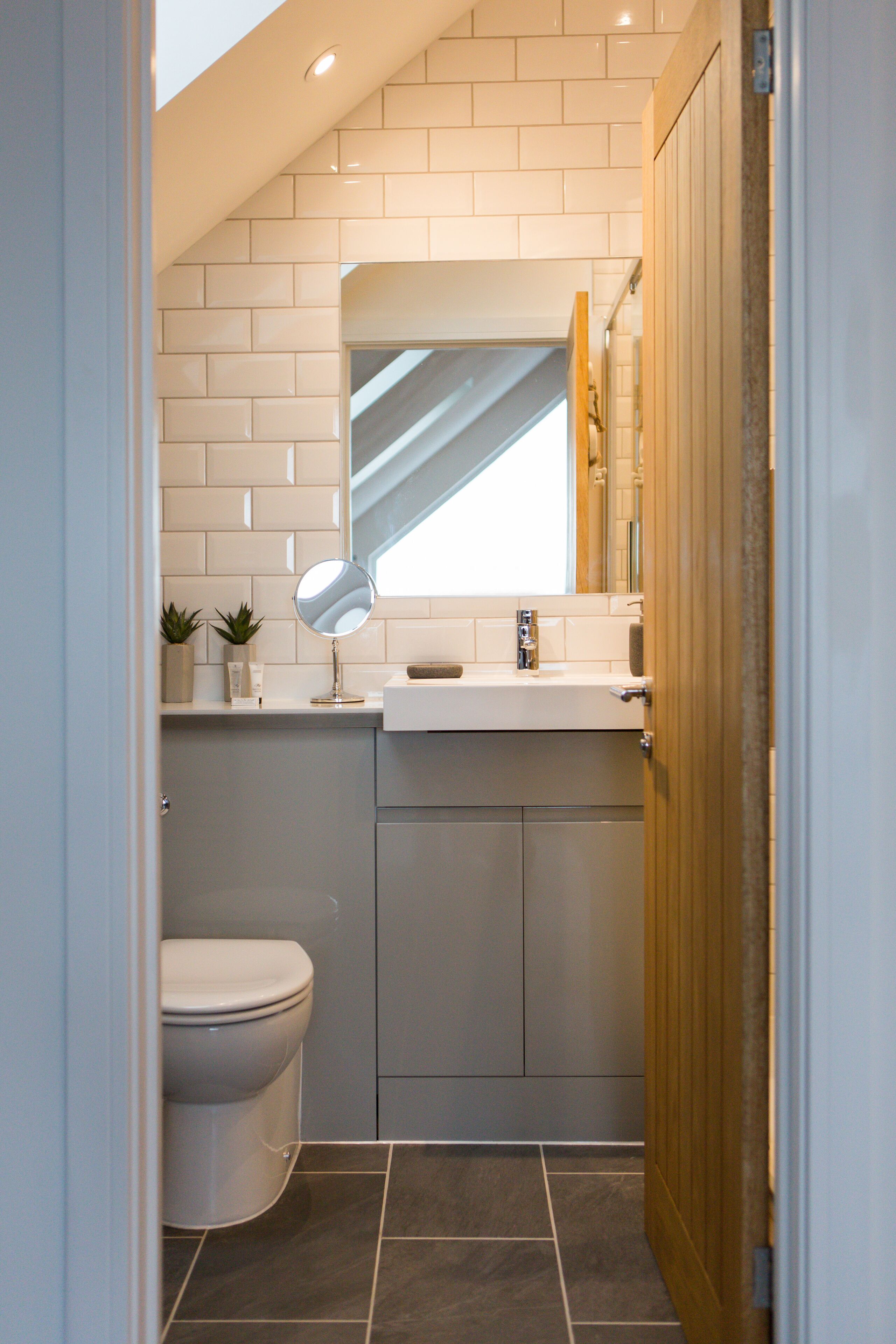 A compact bathroom with a white toilet, a small sink with a mirror, and a window above the sink.