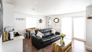 A modern living room with a black leather sofa, a wooden coffee table, and a dining area with a white table and chairs. - The Lighthouse (St Ives)