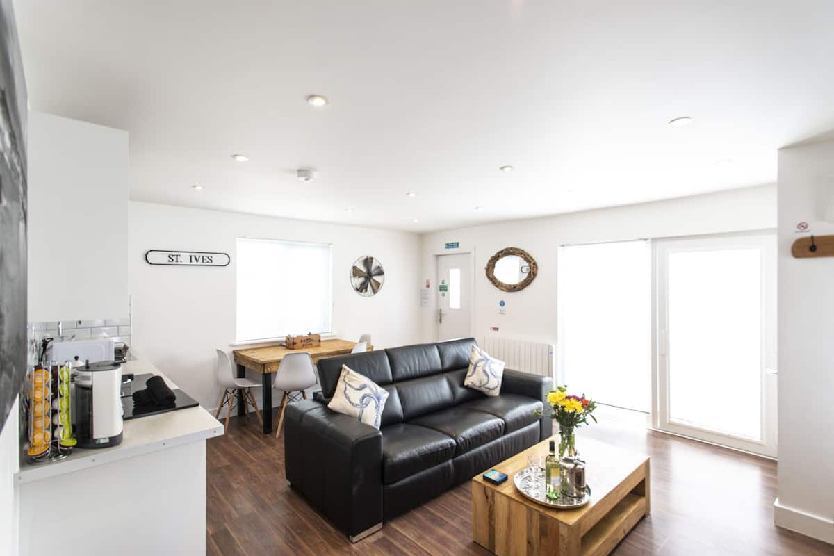 Un salon moderne avec un canapé en cuir noir, une table basse en bois et un coin repas comprenant une table et des chaises blanches.