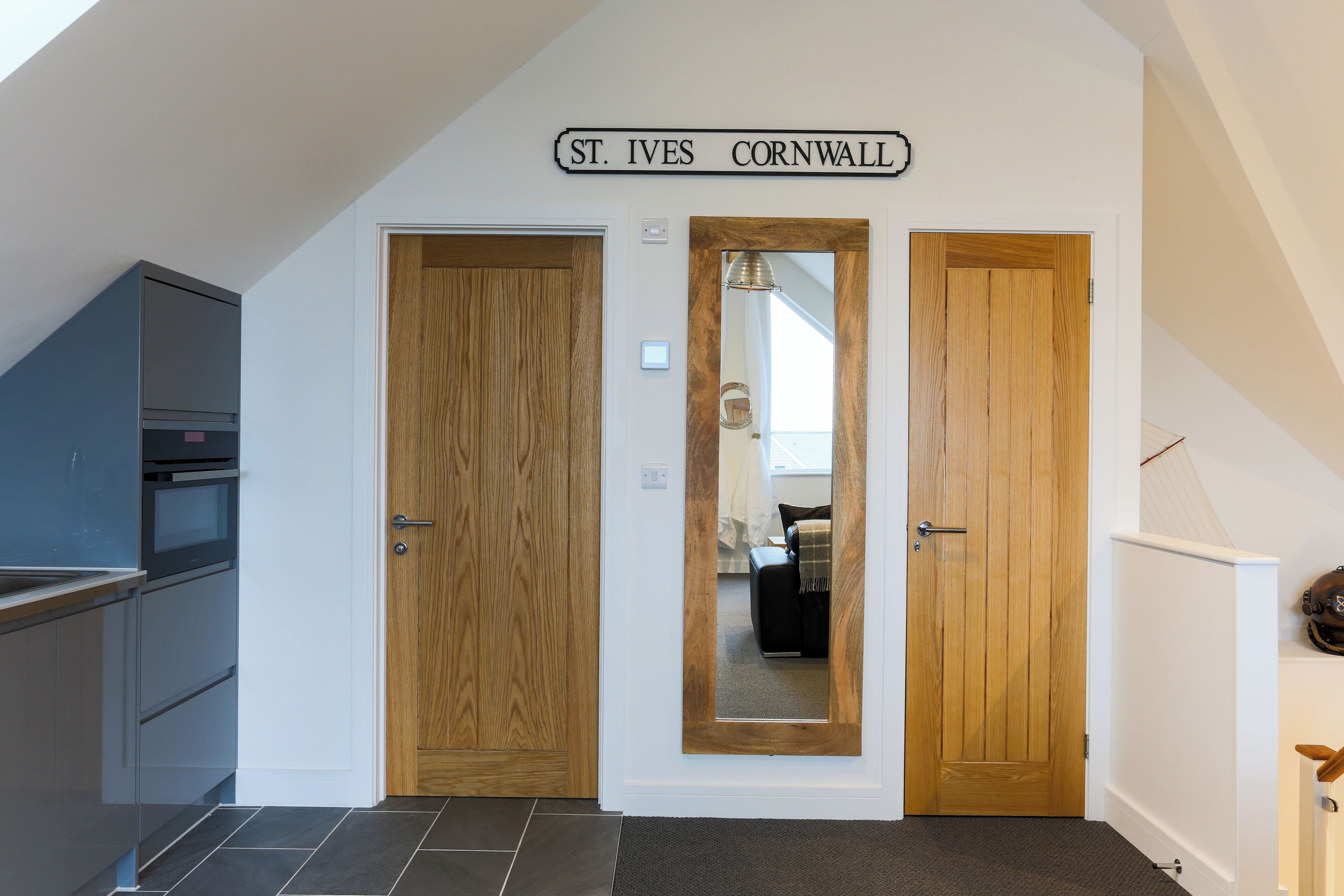 A hallway with two wooden doors, a kitchen area, and a sign reading "St. Ives Cornwall".