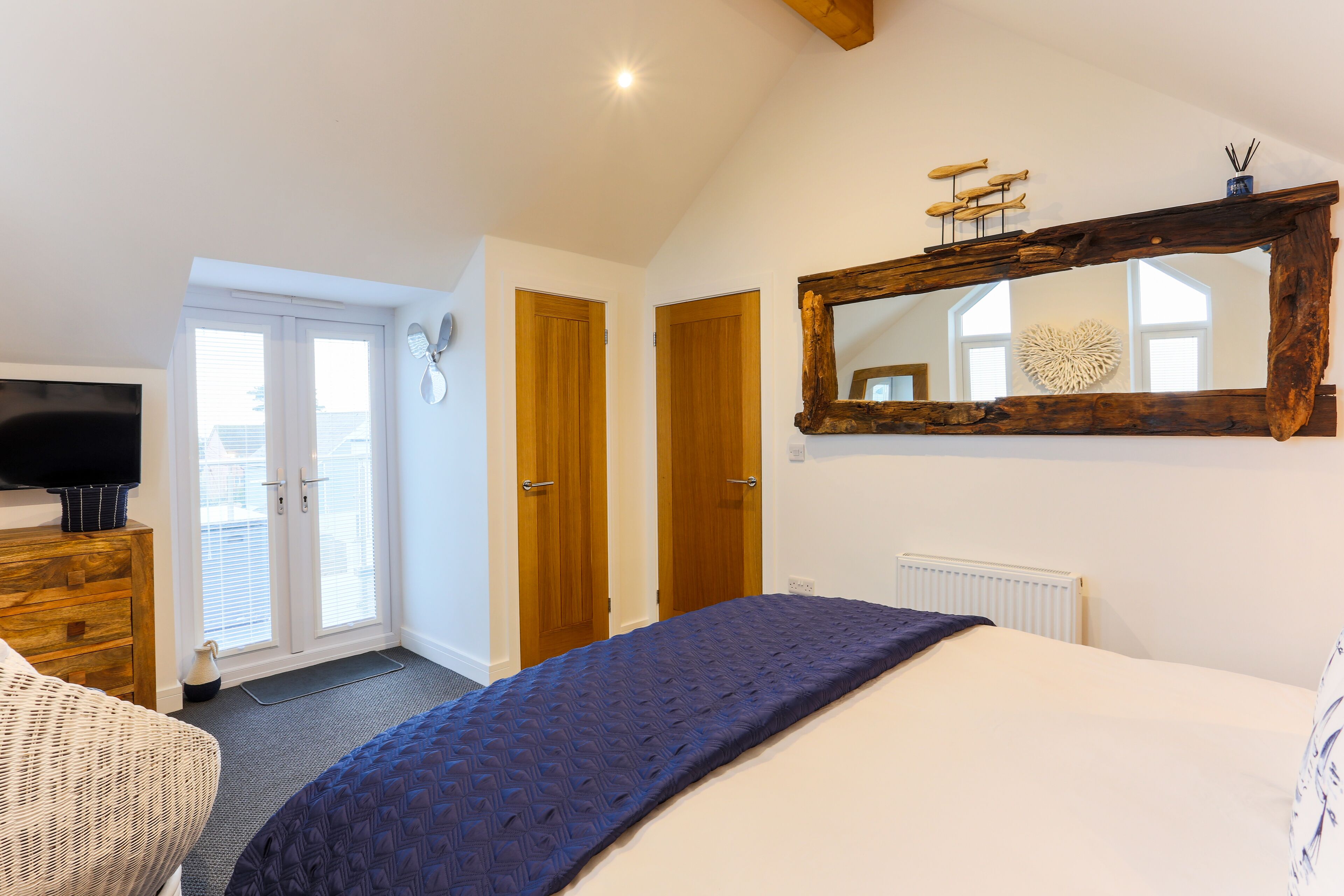 A bedroom with a bed, a wooden dresser, a television, and a large mirror.