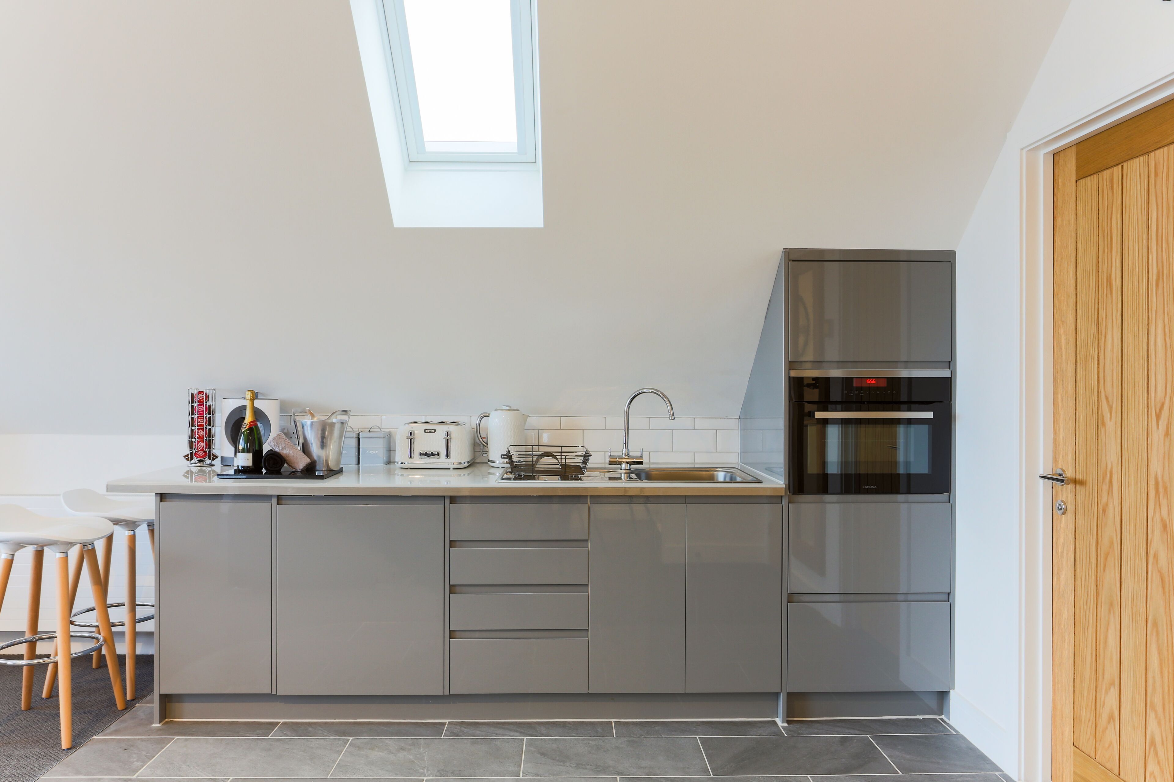 A modern kitchen with a skylight, a built-in oven, and a wooden door.