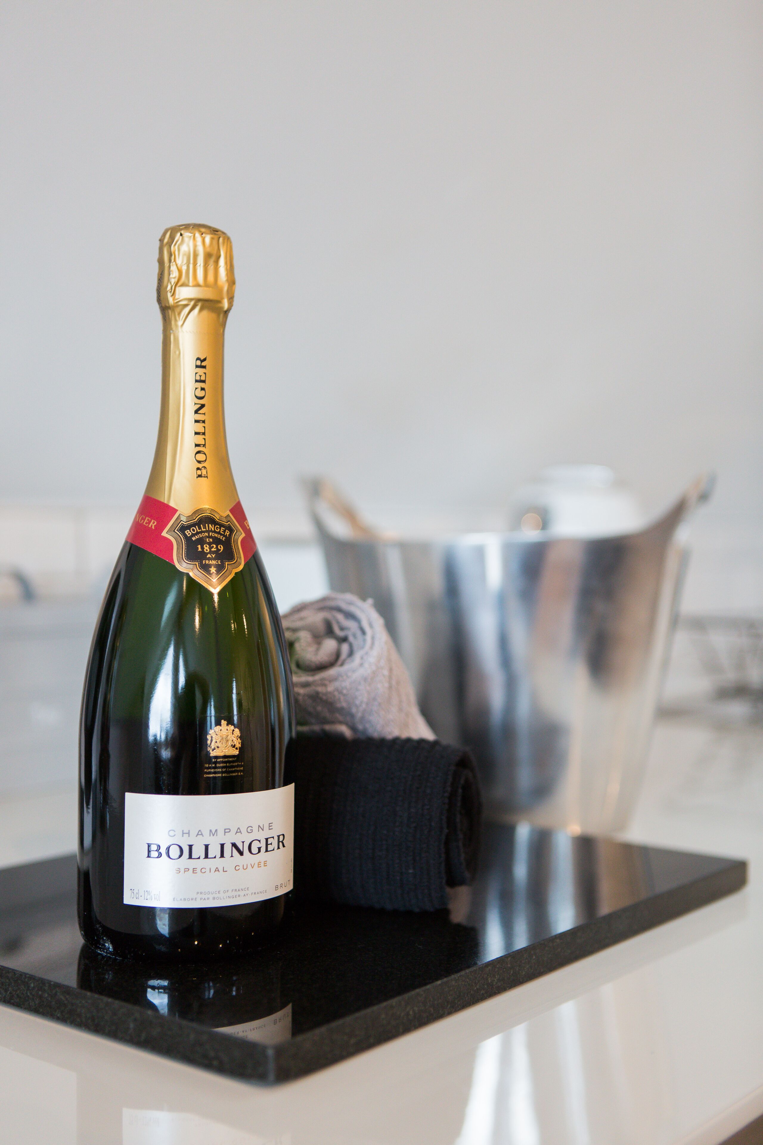 Une bouteille de champagne Bollinger posée sur un plan de travail de cuisine, avec une casserole en acier inoxydable en arrière-plan.