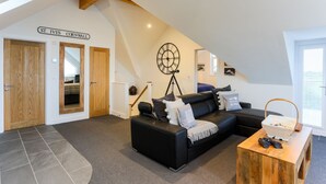 A loft-style living room with a black leather sofa, a wooden coffee table, and a large clock on the wall. There are two wooden doors and a staircase leading to another level. - The Lighthouse (St Ives)