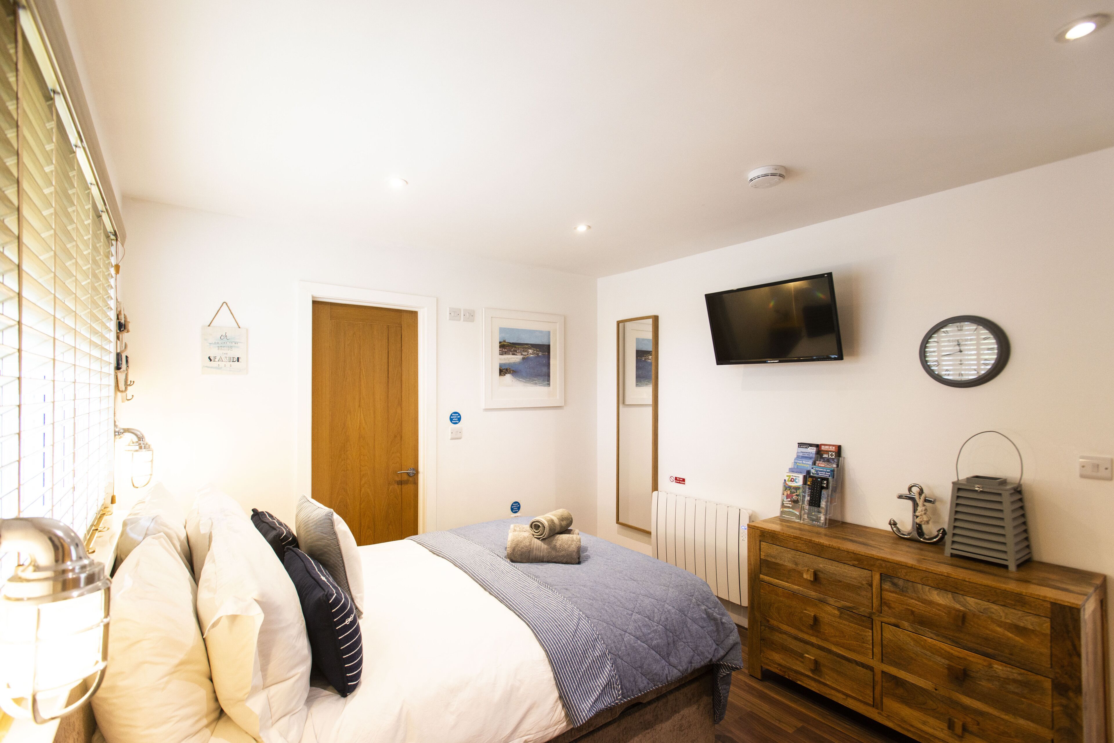 Une chambre à coucher avec un lit, une commode en bois et un téléviseur fixé au mur.