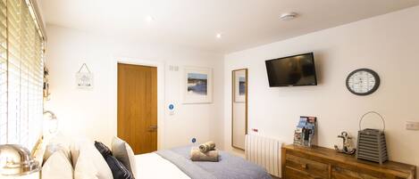 A bedroom with a bed, wooden dresser, and a TV on the wall.