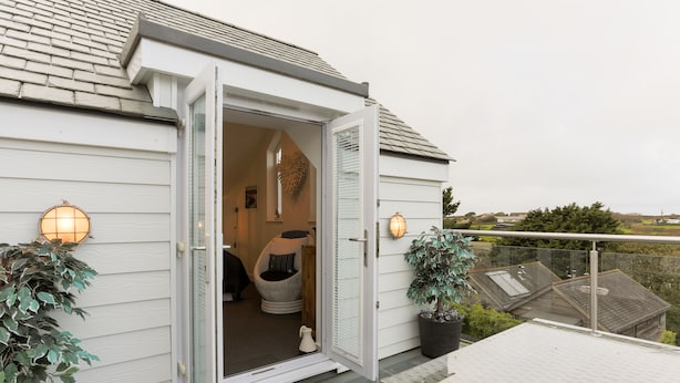 A house with a sliding glass door open to a porch, a potted plant, and a wicker chair. - The Lighthouse (St Ives)