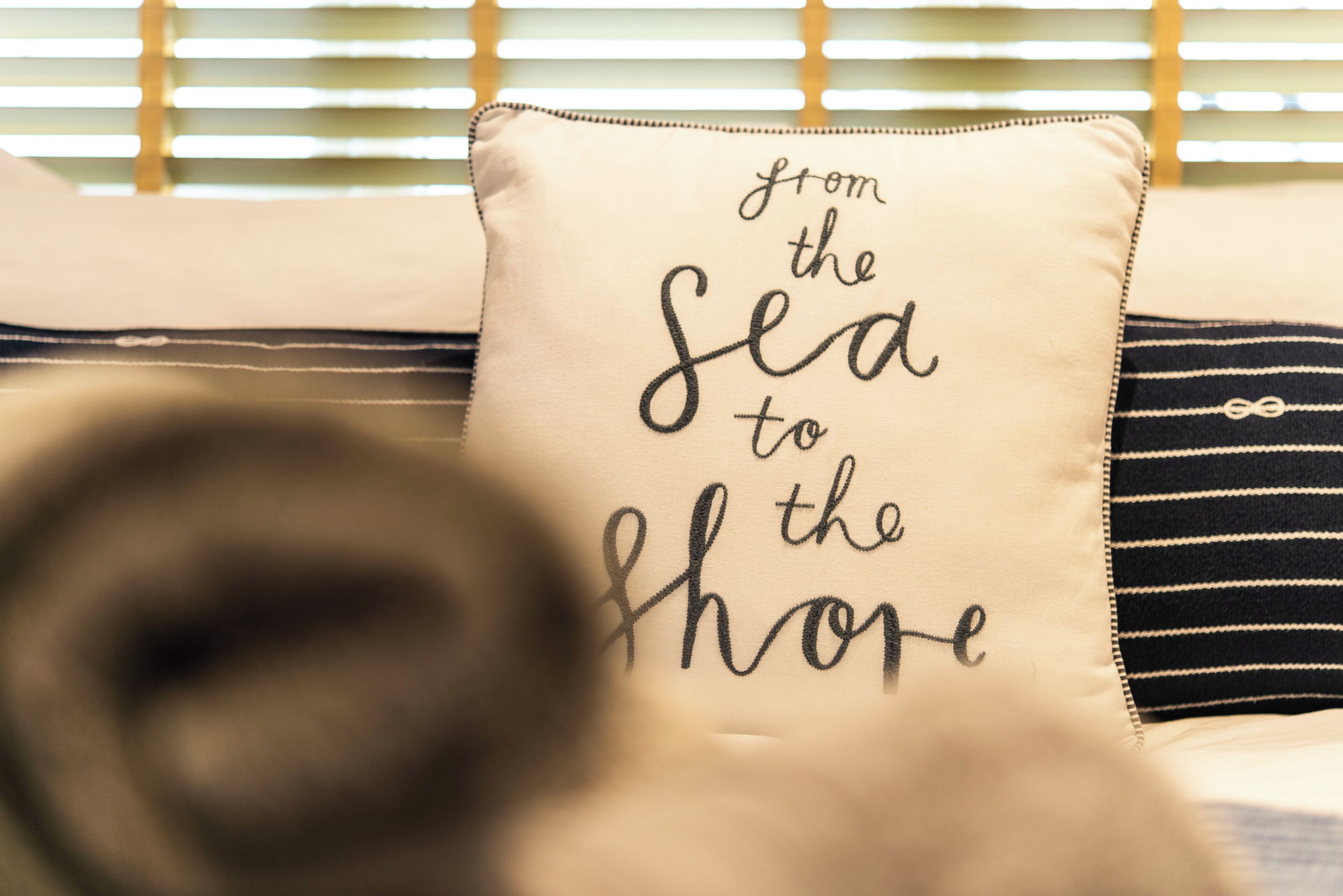 A pillow with the text "from the sea to the shore" on a bed with striped pillows.