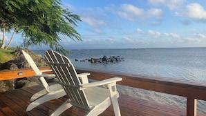 A wooden deck with a white Adirondack chair facing a rocky shoreline and ocean. - Vale Sekoula, Private Villa on the Ocean with Pool and Air Conditioning (matei)