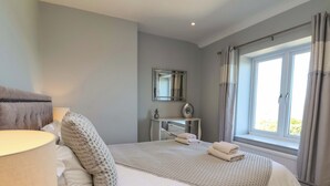 A bedroom with a bed, a bedside table, a mirror, and a window with curtains. - Voebroch (Whitby)