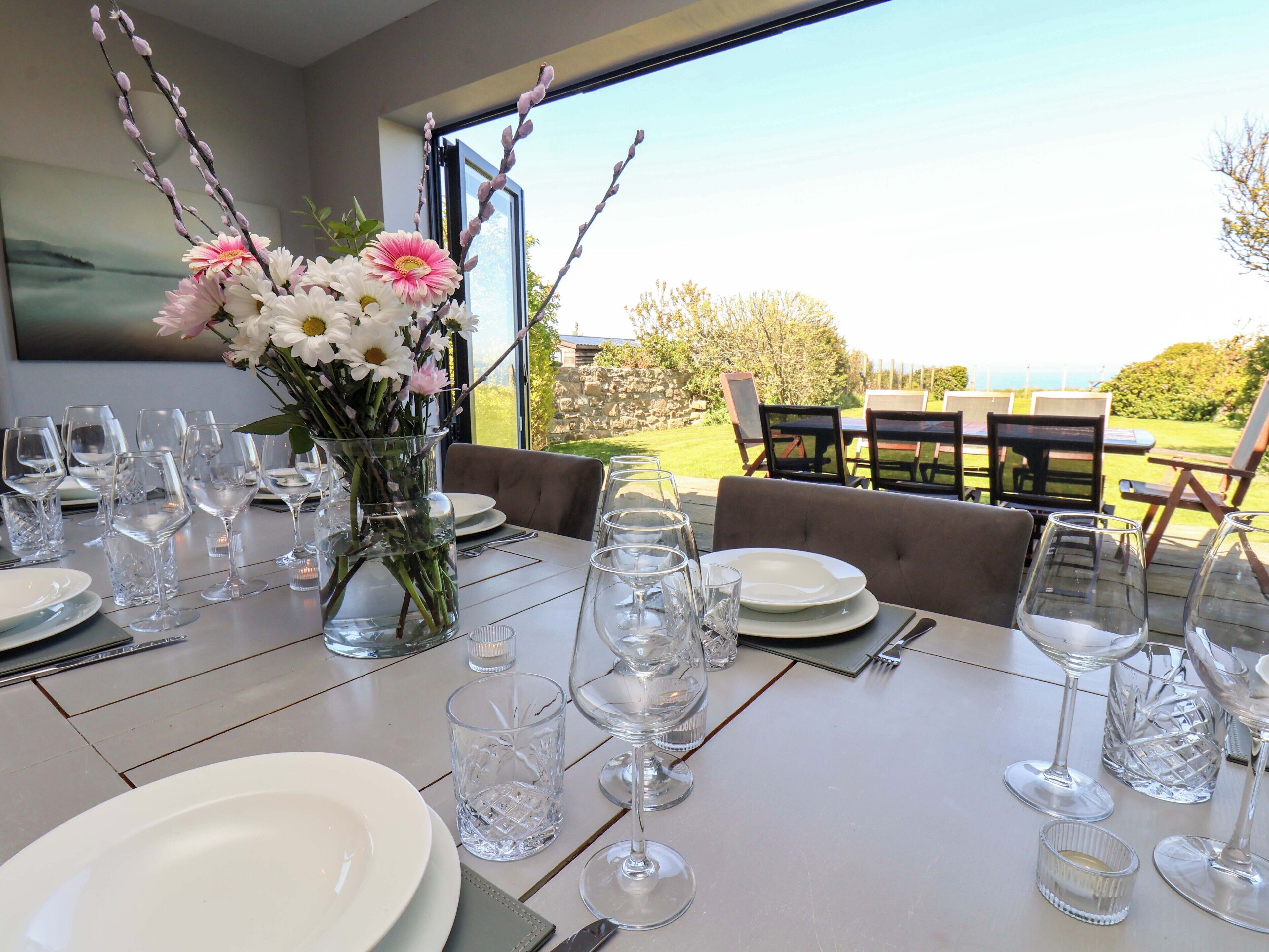 A dining table set with wine glasses, plates, and a vase of flowers.