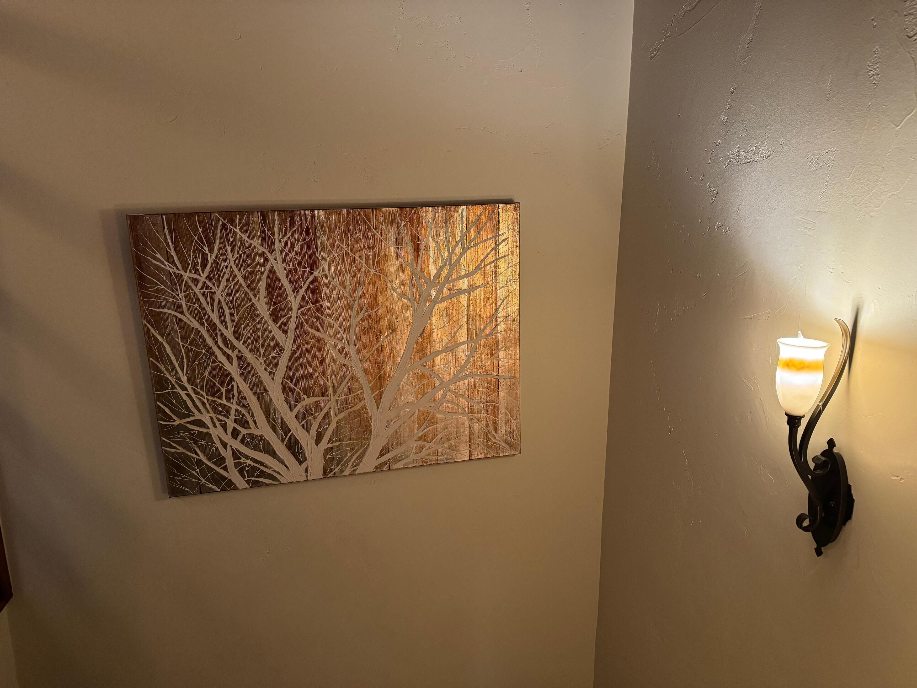 Een muur met een ingelijst abstract schilderij en een wandlamp.