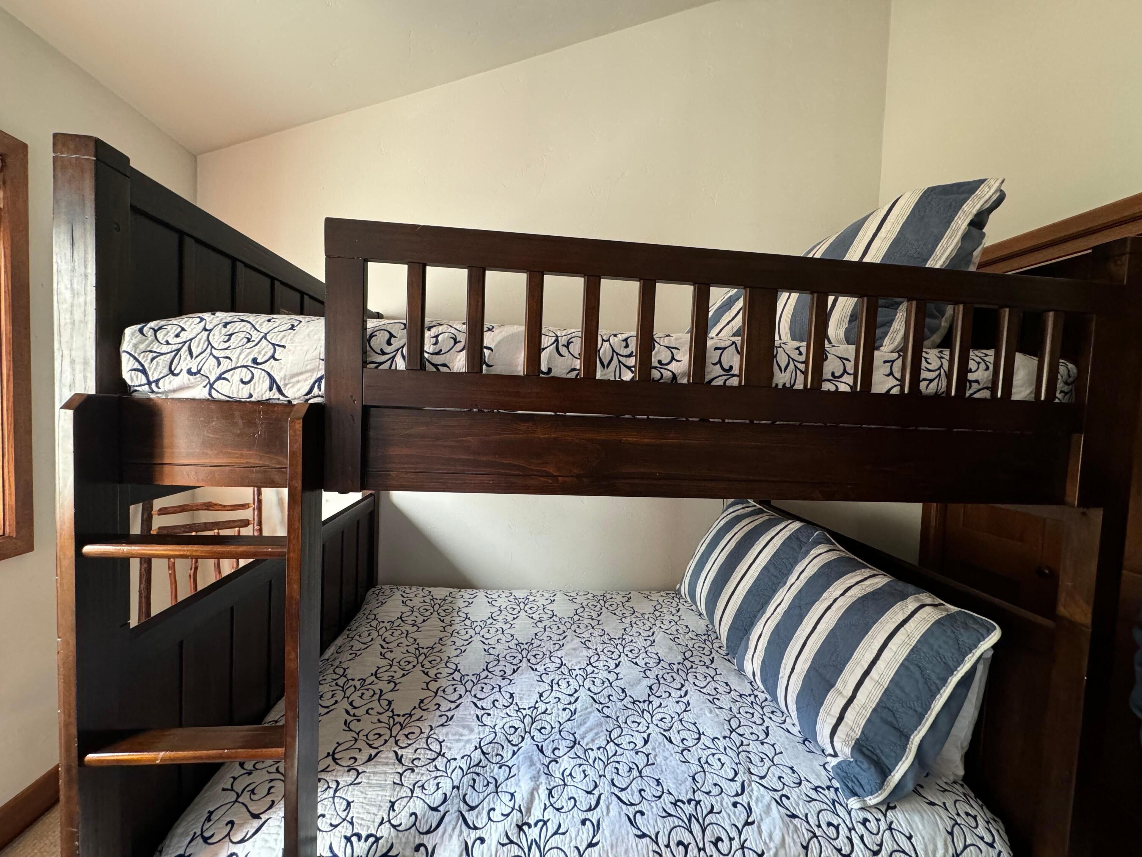 Een stapelbed met een bekleed matras en kussens, een houten hoofdbord en een stoel.