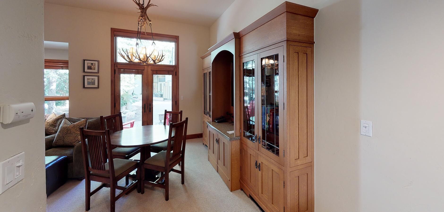 A dining area with a wooden table and chairs, a chandelier, and a cabinet with glass doors.
