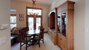 Een eetruimte met een houten tafel en stoelen, een kroonluchter en een kast met glazen deuren.